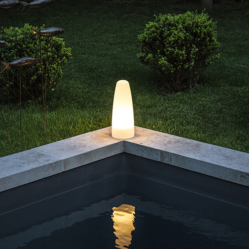 Luminaire en forme de lanterne posé en bord de piscine à la tombé de la nuit.